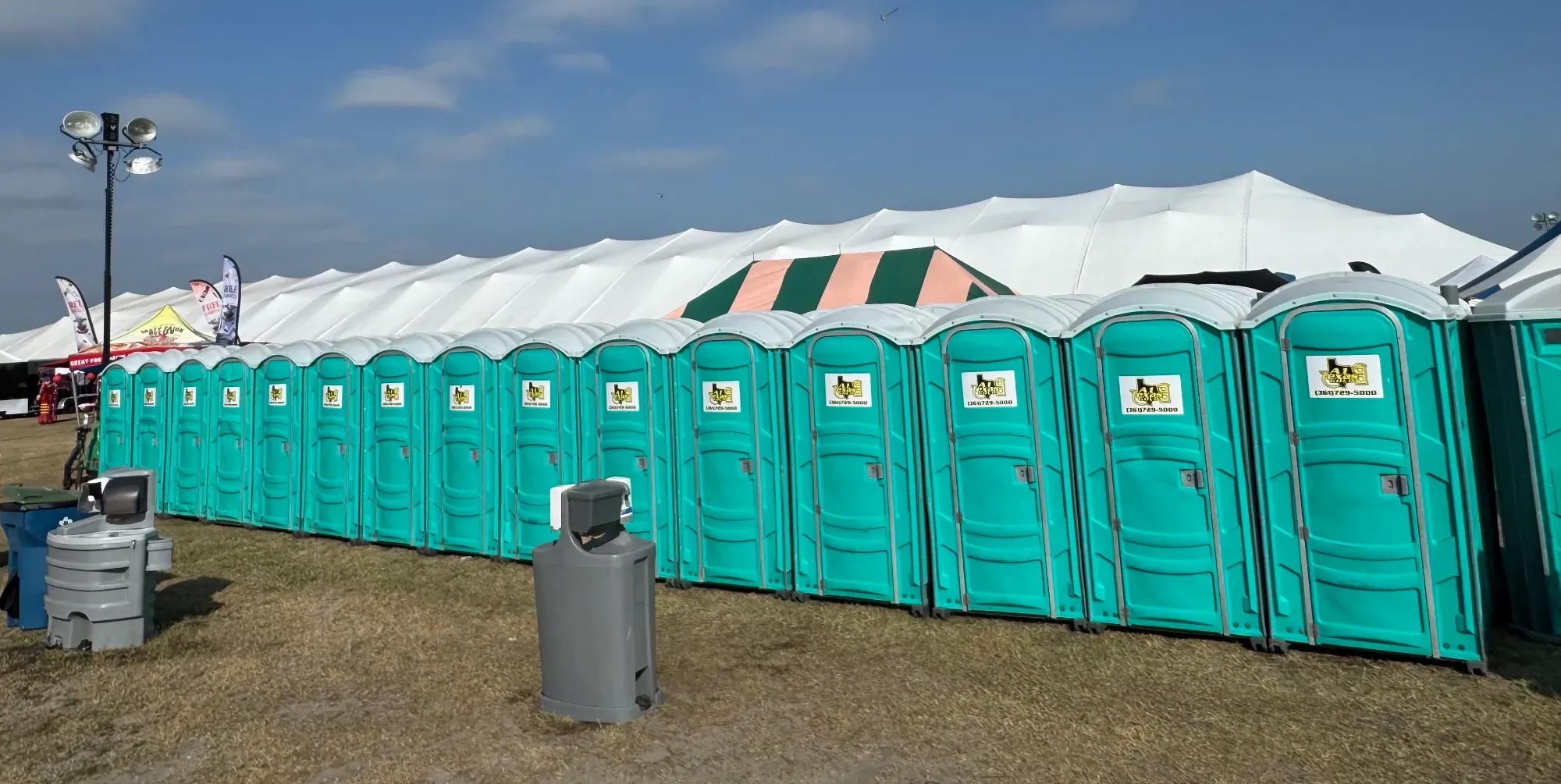 Long row of A1 Texas Gold event porta potties beside a festival tent
